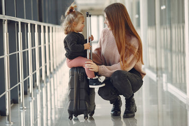 Lachende Mutter und Tochter sitzen mit ihrem Koffer im Flughafen-Terminal - Kinderkoffer Ratgeber: Größe, Gewicht und handgepäcktauglich